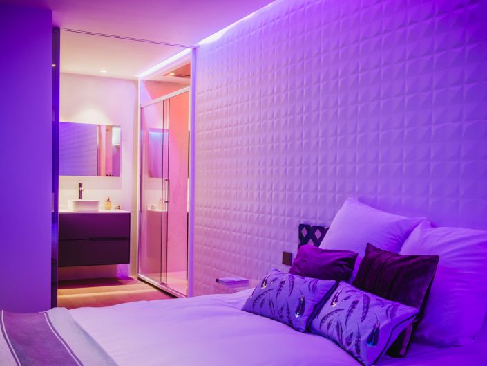 Cabecero de la cama en tonos morados en habitacion con baño en suite de un hotel boutique en Madrid